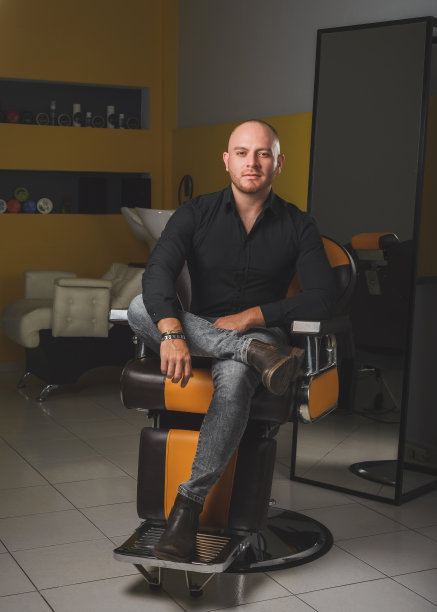 一个理发师坐在他工作场所的理发师椅子上的画像。图片下载