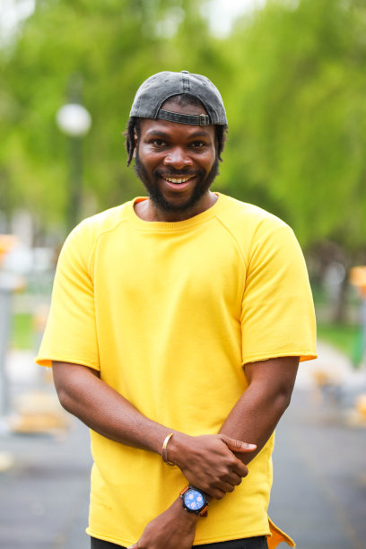 年轻的黑人男子戴着黄色衬衫的帽子在绿色背景前的肖像图片下载