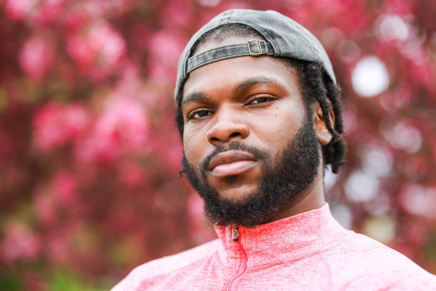 戴着帽子的黑人男子站在粉红色盛开的树前的特写肖像图片下载
