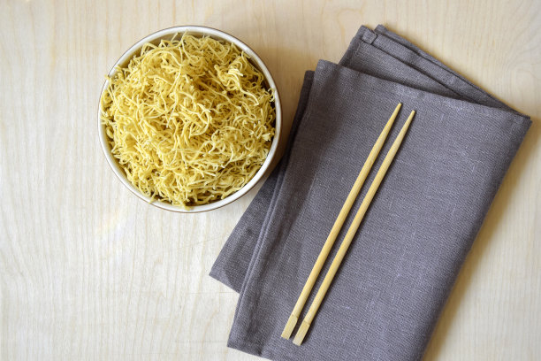 自制煮面，平铺。生意面在碗里。轻木表面主要成分、成品和一次性山毛榉木筷子。灰色的餐巾。前视图。图片下载