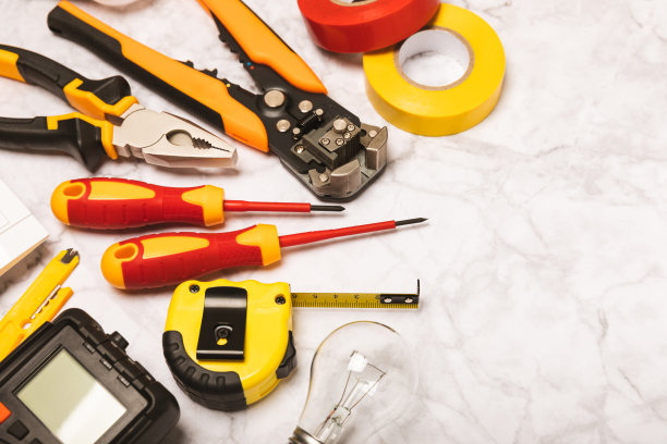 电工工具，白色大理石背景。万用表，施工胶带，电工胶带，螺丝刀，钳子，自动绝缘剥离器，插座和LED灯。弗拉特利。电工概念。工具箱。图片下载
