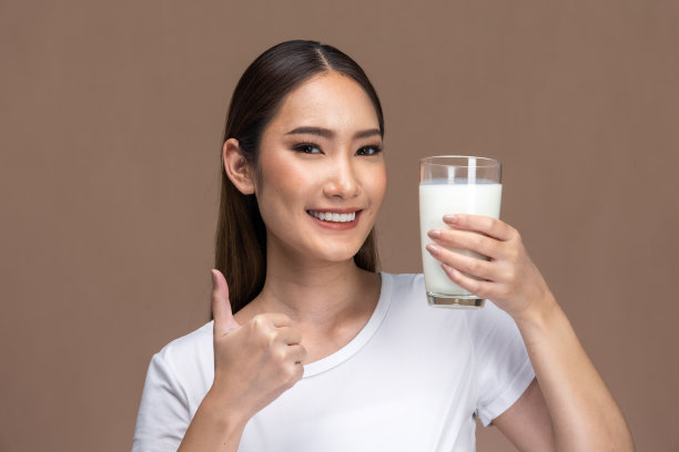 亚洲美女可爱的女孩感到快乐，喝牛奶为身体健康幸福米色背景。图片下载