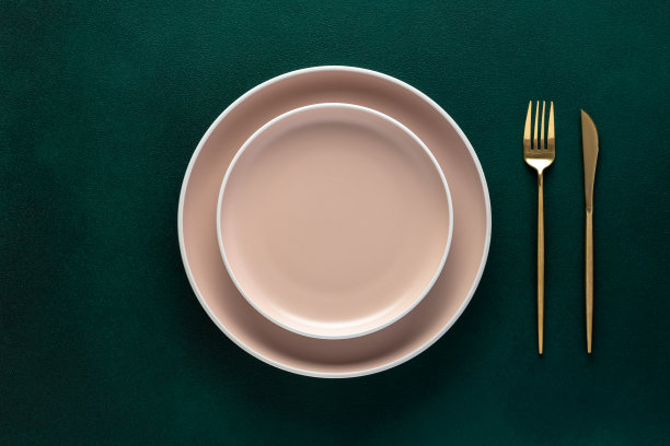 空的米色盘子，深绿色背景上的金色刀叉。俯视图，复制空间。表设置。平面设计。图片下载