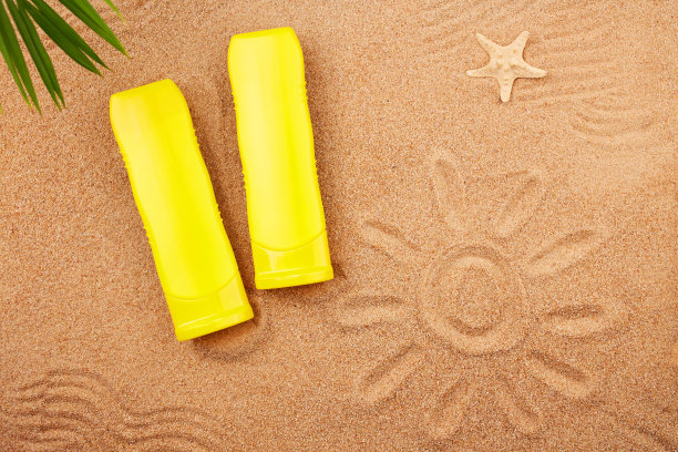 夏天的背景。几管防晒霜和沙滩上的一片棕榈叶。图片下载