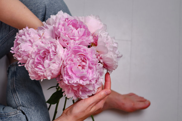 快乐的女人手里拿着粉红色的牡丹。卖花的女孩收集了一束牡丹。娇嫩的花朵很美。一份节日礼物，春天心情。浪漫的惊喜图片下载