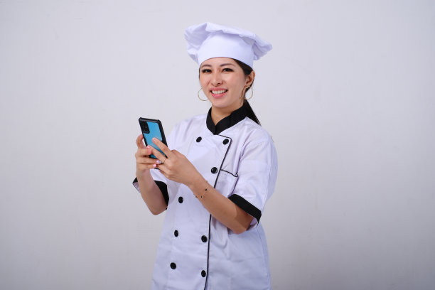 快乐微笑的亚洲女厨师在孤立的白色背景上使用手机图片下载