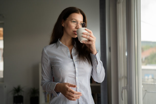 一个白人妇女站在窗前端着一杯咖啡图片下载