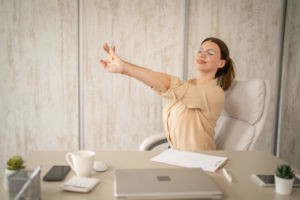 商务女性在办公室工作时坐在办公桌前做伸展运动图片下载