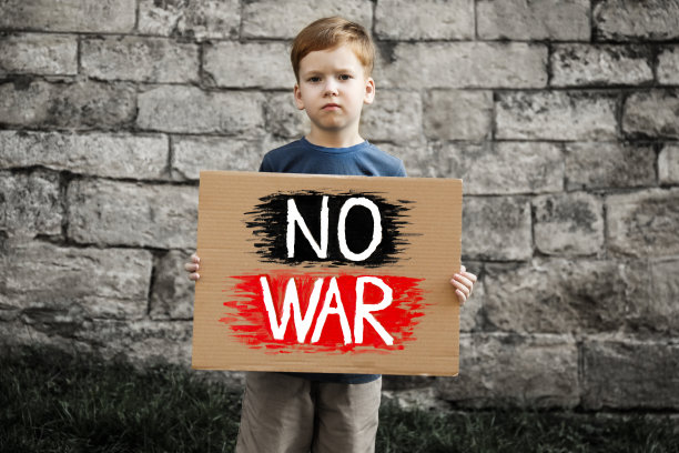 悲伤的男孩举着海报，上面写着“不要战争”在外面的砖墙上图片下载