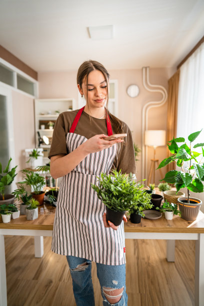 一名年轻女子正在用智能手机照顾植物和拍照图片下载