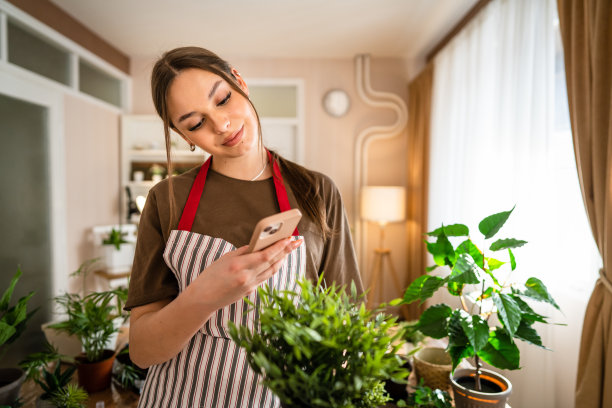 一名年轻女子正在用智能手机照顾植物和拍照图片下载