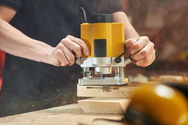 高加索工人用电动铣刀在木坯上刻槽，木屑向不同方向飞散图片下载