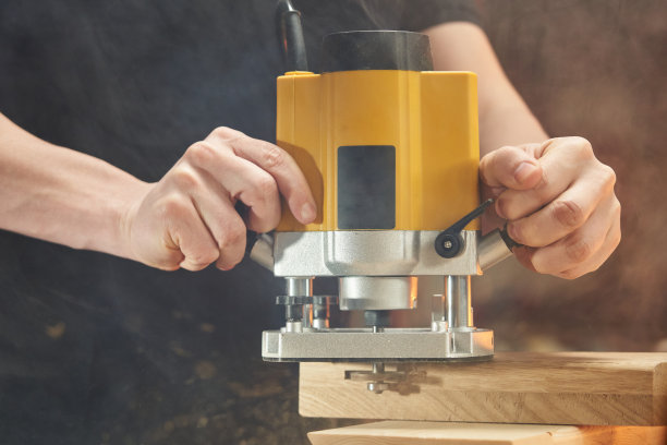 白人工人驾驶电动铣刀的特写。木制品上的凹槽图片下载