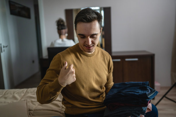 一名白人夫妇在酒店房间收拾或从行李箱中取出衣柜布，而他的妻子或女朋友坐在后台旅行和度假概念复制空间图片下载