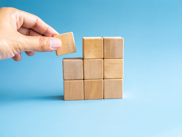 最后一块木块放在手中的木块拼图上堆叠排列，在蓝色背景上完成孤立，风格极简。解决方案，解决问题，业务目标和成功计划的概念。图片下载