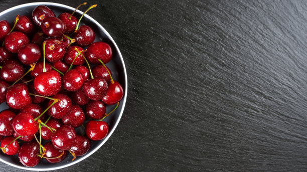 新鲜的红色成熟的甜樱桃盘黑色石板背景。图片下载
