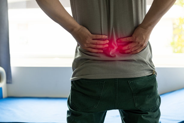 穿着灰色t恤的不快乐的年轻人患有严重的背部疼痛触摸你的背部，试图减轻你脊椎的疼痛。特写照片图片下载