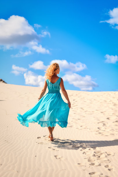 美丽的金发女子在炎热的沙滩上，蓝天为背景。图片下载