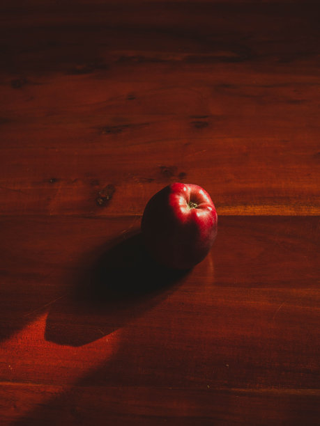 一个红苹果和它在木桌上的影子的垂直静物画图片下载