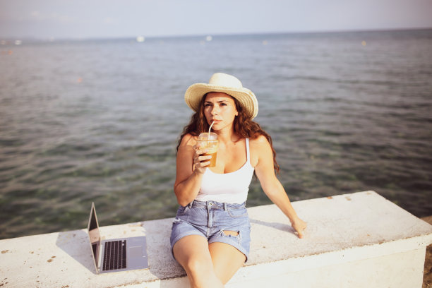 年轻女子在海滩上用笔记本电脑工作的照片图片下载