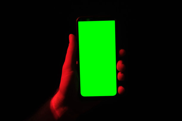年轻人手里拿着手机。使用绿屏的智能手机配红蓝霓虹灯，背景暗。男性显示黑色手机色度键显示。关闭了。手抬起设备，保持它不动图片下载