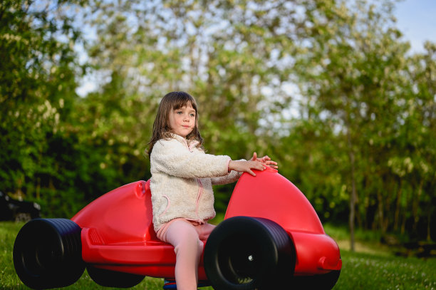 在户外操场上，一个学龄前女孩坐在一辆红色的汽车里。图片下载