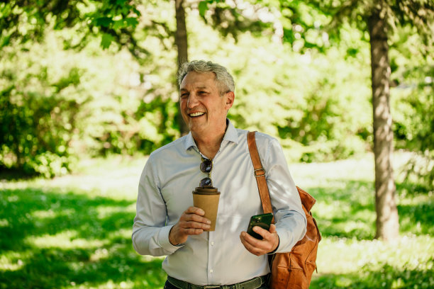 背着背包的资深商人在公园里散步，一边看手机。图片下载