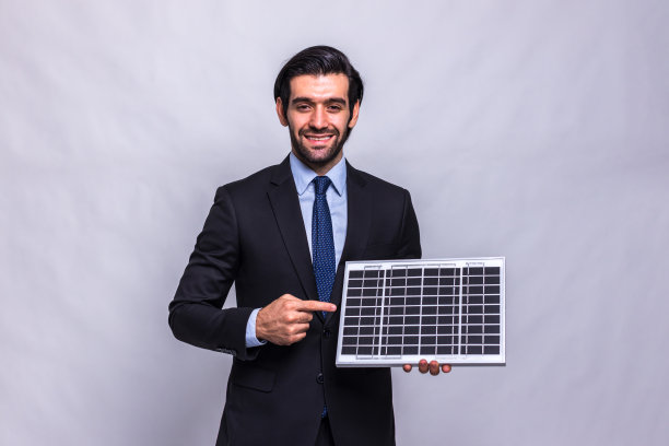 拿着太阳能电池板的商人。微笑的男工程师拿着一块隔离在白色背景上的光伏太阳能板。人们在讨论太阳能发电环境图片下载
