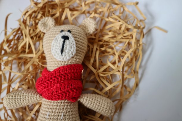 钩针编织可爱的泰迪熊与红色围巾与片棕色纸在白色的背景。钩针的洋娃娃。手工编织，艺术和工艺的概念。图片下载