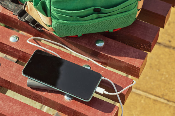 充电宝可以在一个绿色袋子的长椅上给智能手机充电。小玩意的便携式充电器。图片下载