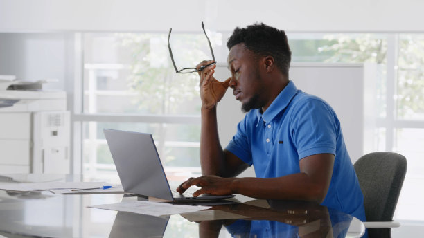 在现代办公室里，疲惫的年轻商人带着笔记本电脑坐在办公桌前过度工作图片下载