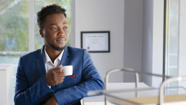 快乐的非洲商人在办公室休息，站在窗前喝咖啡，做白日梦图片下载