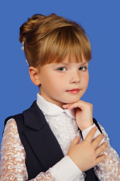 可爱的8-9岁的女学生在学校形象衣在孤立的蓝色背景，看着镜头。小学生，小女孩，画室肖像。学生的概念。复制广告文本空间图片下载