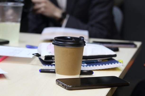 一个带盖子的纸杯，咖啡外带。咖啡杯放在办公室桌子上，背景是黄色的图片下载