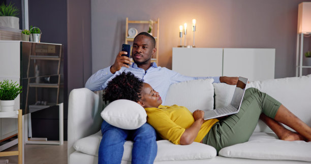 年轻夫妇在沙发上使用笔记本电脑和手机图片下载