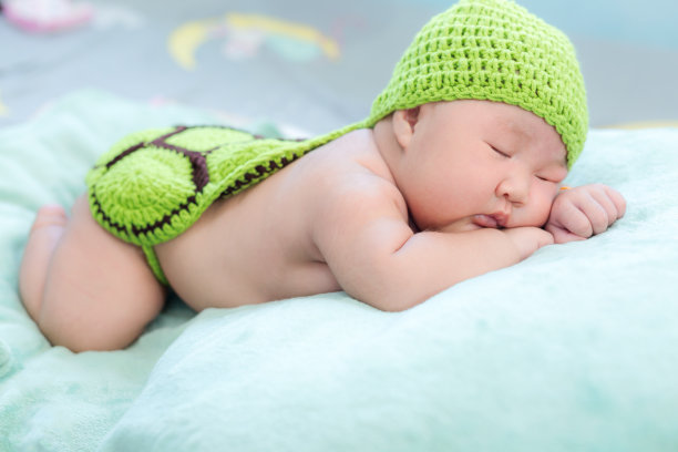 一个一个月大的新生儿躺在一条毛巾上，在绿色的连衣裙下放松。图片下载