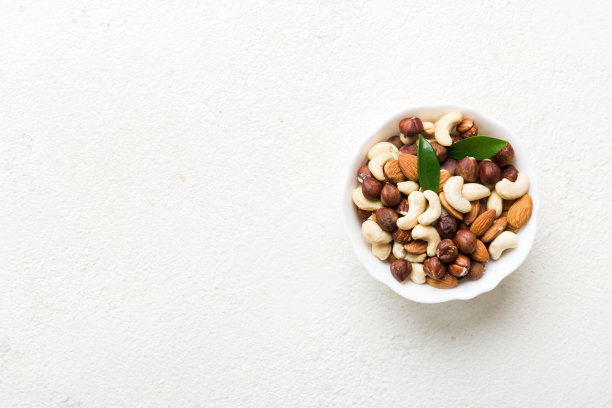 五颜六色的桌子上，木碗里有各式各样的坚果。腰果，榛子，核桃，杏仁。顶部视图与复制空间的混合图片下载