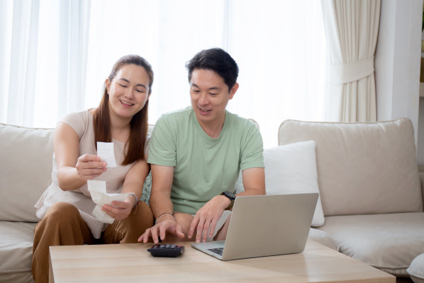 幸福的家庭，一对夫妇坐在沙发上，在家里的客厅里一起计算家庭的财务和开支，男人和女人核对账单和发票，了解成本、生活方式和储蓄观念。图片下载