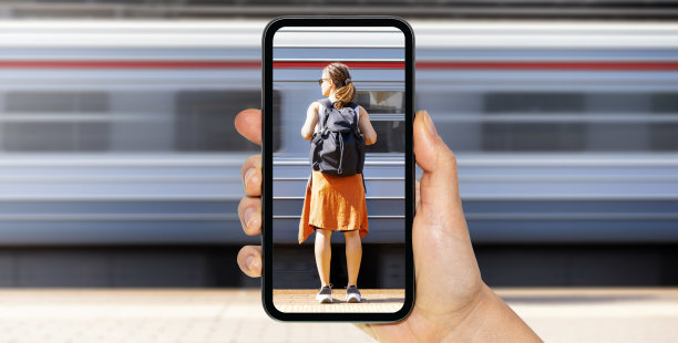 一名女乘客站在火车站站台上，手里拿着触摸屏手机。图片下载