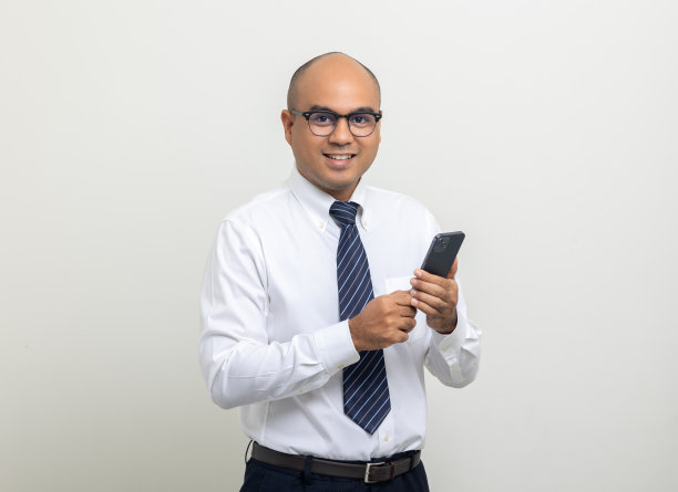 年轻的亚洲商人在孤立的白色背景上使用手机的肖像。英俊的中年印度商人穿着办公室制服拿着智能手机。图片下载