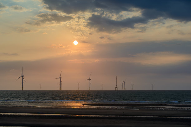 风力涡轮机的风扇在波光粼粼的海面上旋转。日落时的动态云。图片下载