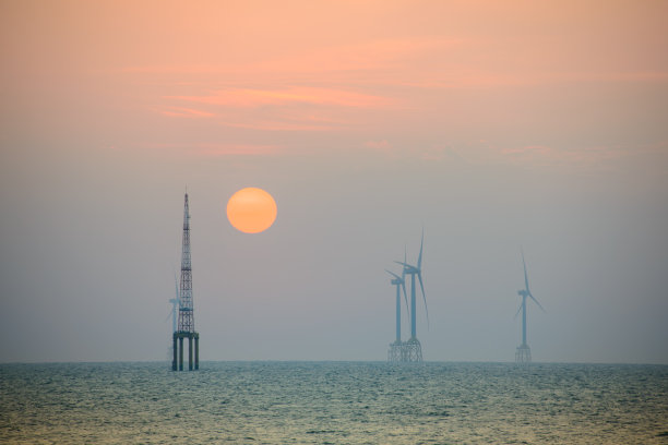 风力涡轮机的风扇在波光粼粼的海面上旋转。黄昏时橙红色的太阳。图片下载