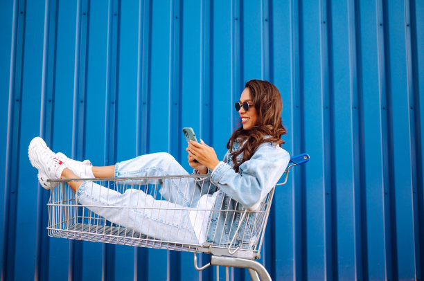 年轻女子拿着手机在购物车里开心地自拍。图片下载