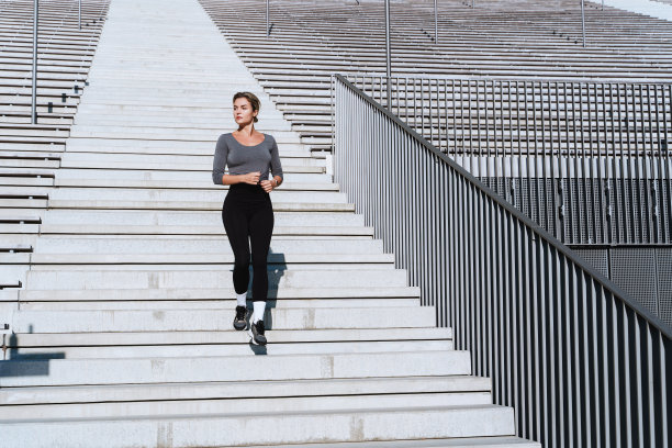 穿着女式运动服的女运动员在室外体育场看台间的楼梯上跑步锻炼图片下载