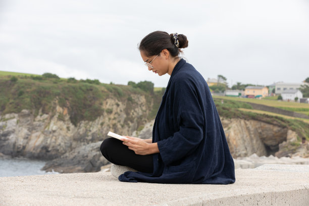 穿便服的女性在海边看书的侧视图图片下载