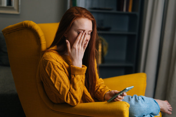 图为，视力模糊、疲惫不堪的年轻女性一边用智能手机打字，一边揉着眼睛、眯着眼睛。图片下载