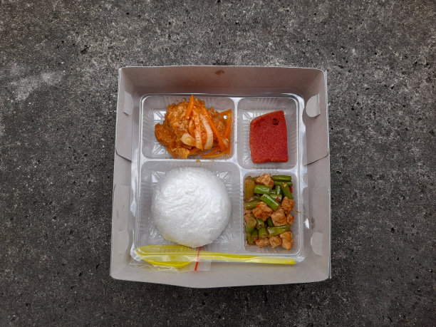 午餐菜单包括白米饭、炸鸡卷、四季豆、以街道纹理为背景的纸盒鸡块。图片下载