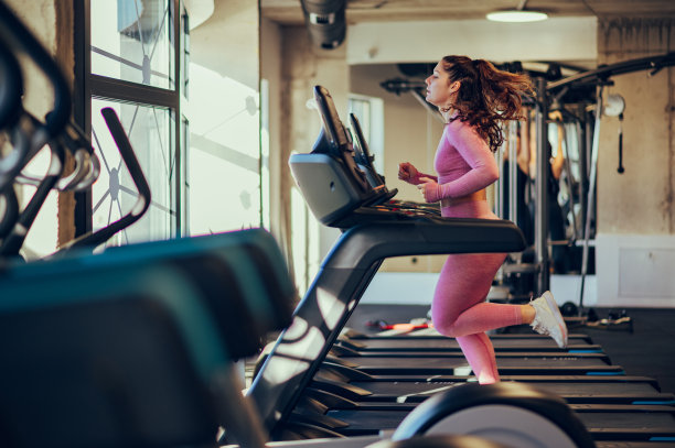 一个年轻的女运动员在健身房里的跑步机上快速奔跑的全长。图片下载