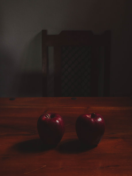 在黑暗的意大利乡村厨房里，两个红苹果和它们在木桌上的影子的垂直静物画图片下载