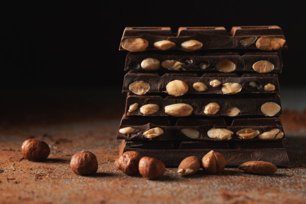 黑巧克力和牛奶巧克力，坚果在深色背景上撒上可可粉。图片下载